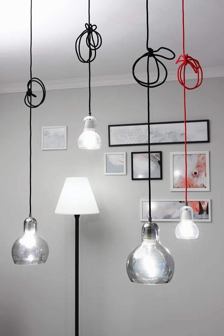 Pendant lamps at various heights with coloured cables and standard lamp against pale grey wall in background