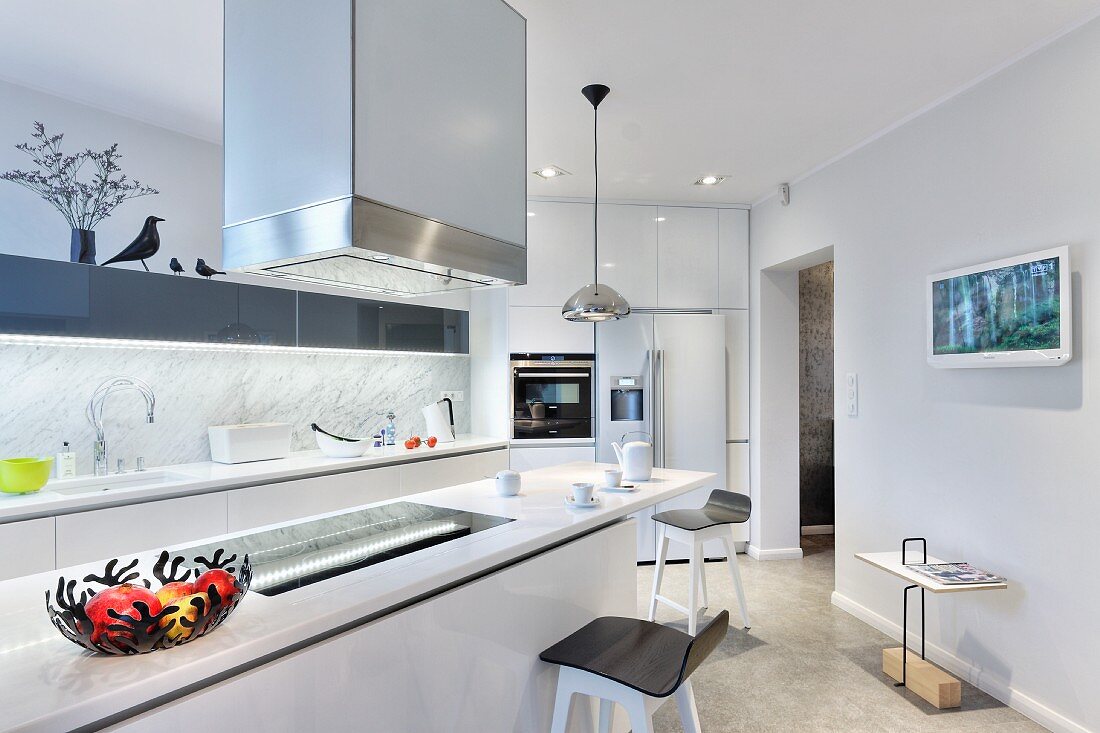 White counter below stainless steel extractor hood and bar stools in designer kitchen