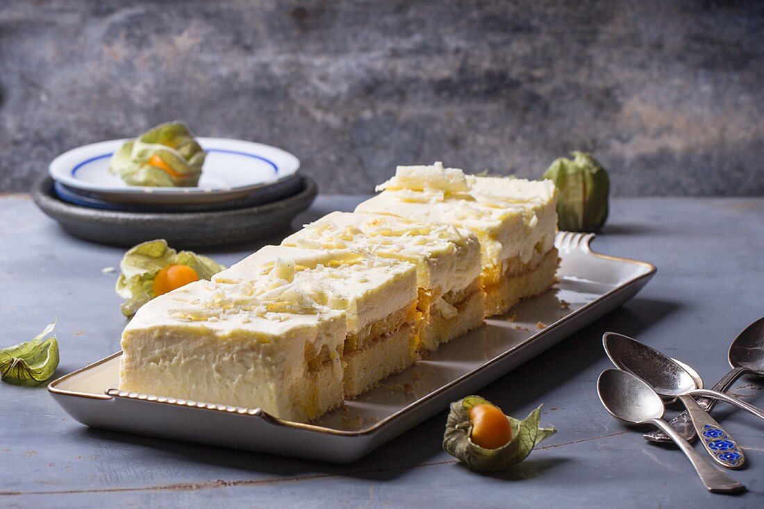 Slices of homemade mango and physalis cake on a serving platter with old teaspoons next to it