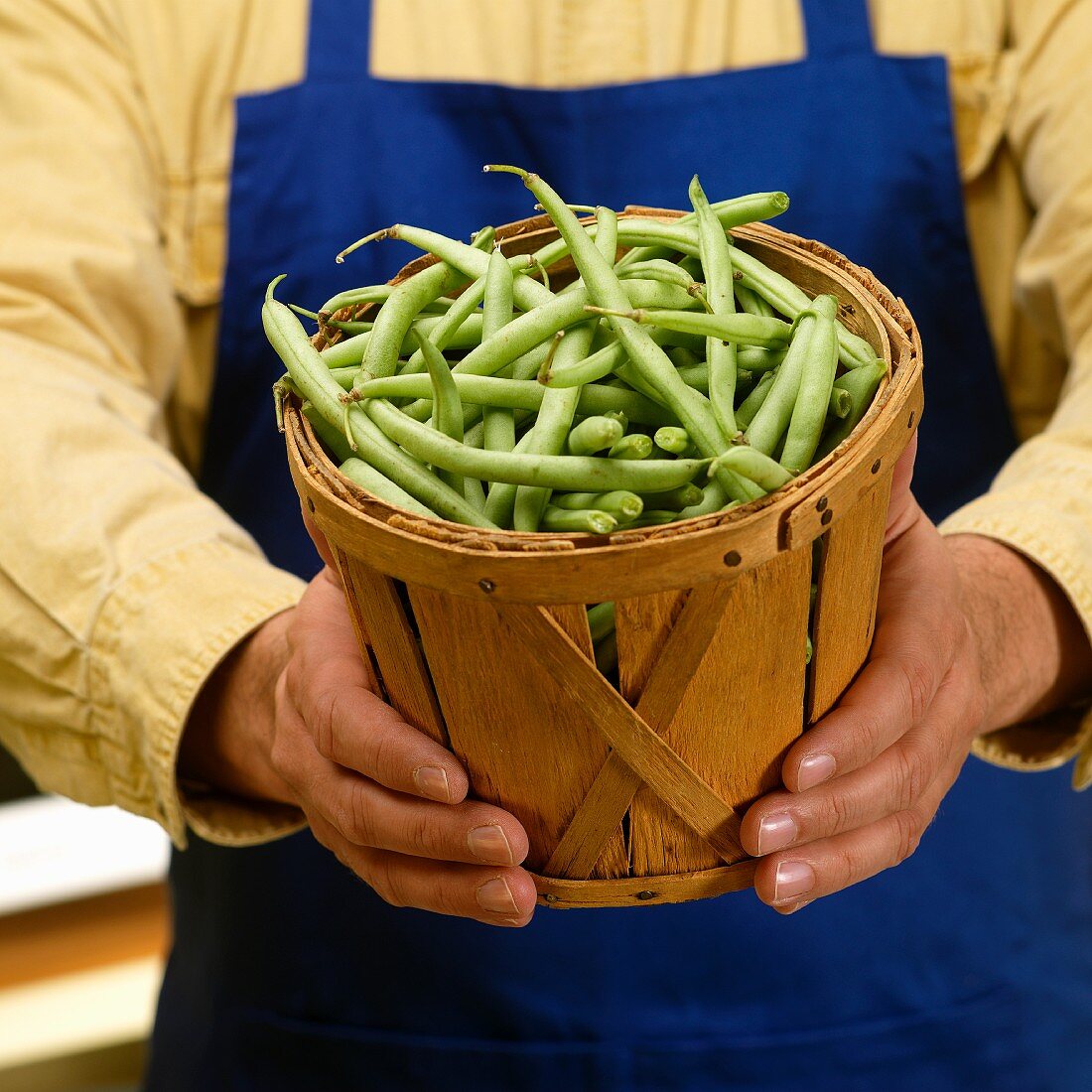 A man holding a wooden basket of green beans
