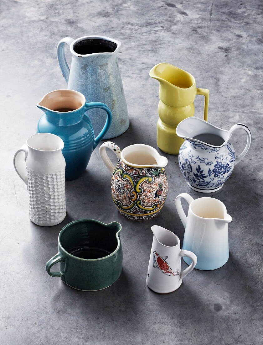 A collection of retro jugs, coloured and patterned, on a concrete floor