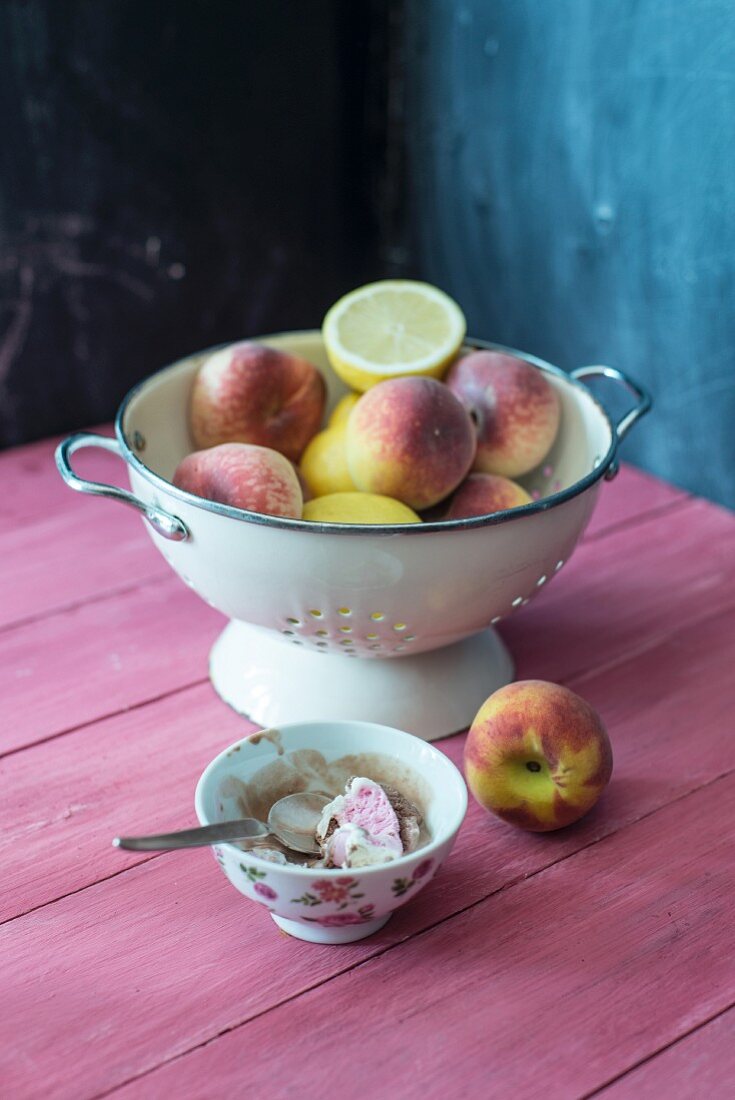 Peaches, vineyard peaches and lemons in a colander with a bowl of Neapolitan ice cream next to it