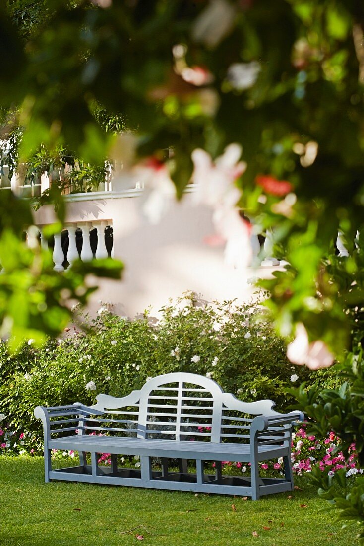 Gartenbank im Garten vor einem Staudenbeet mit Rosen und Petunien