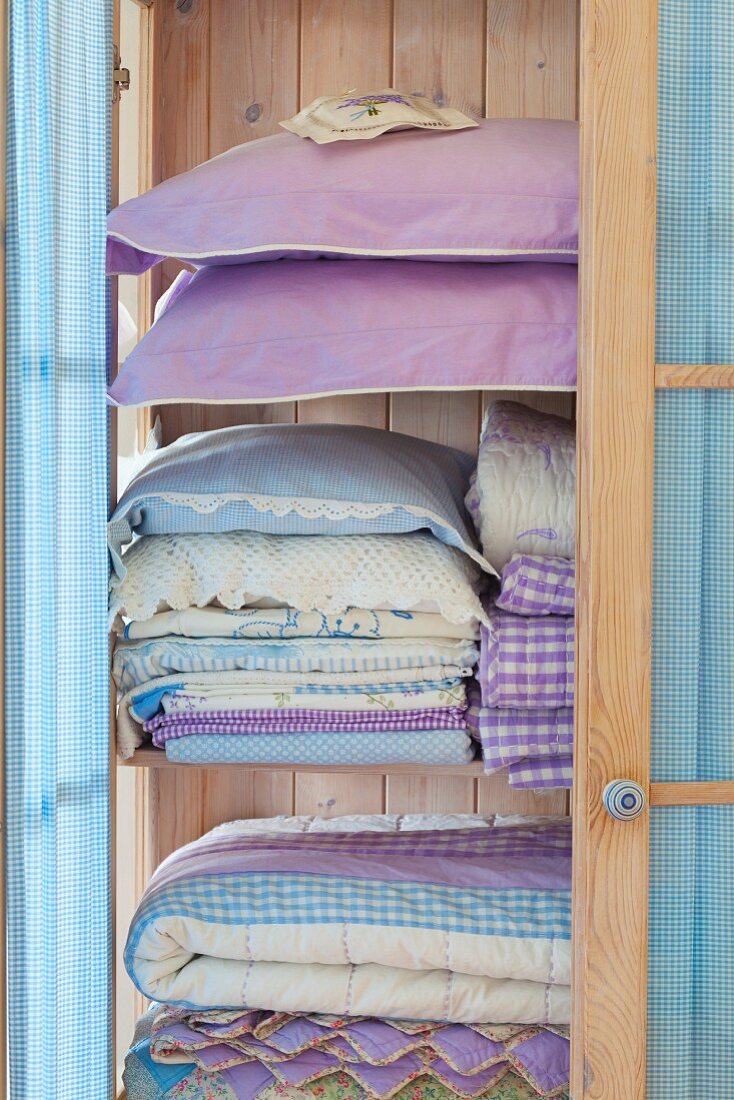 Stacks of pastel-blue bedclothes and pillows in a light wooden cupboard