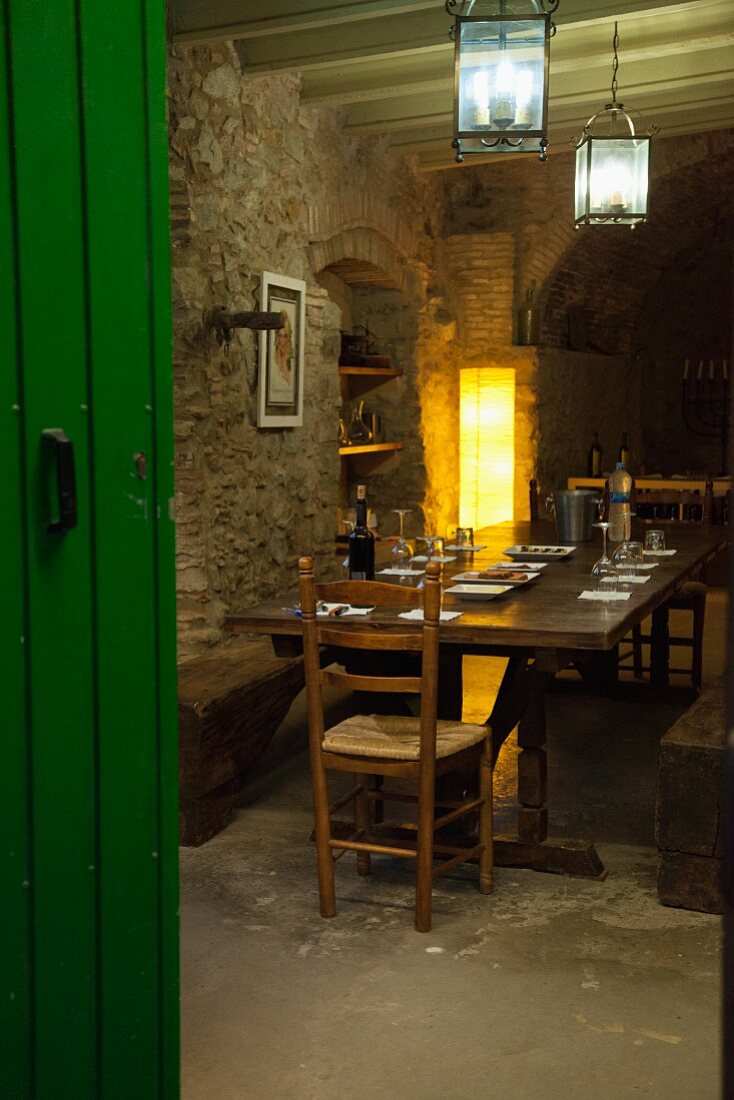 Dark wooden table in dining room with rustic stone walls, standard lamp in corner and wooden shelves in niche