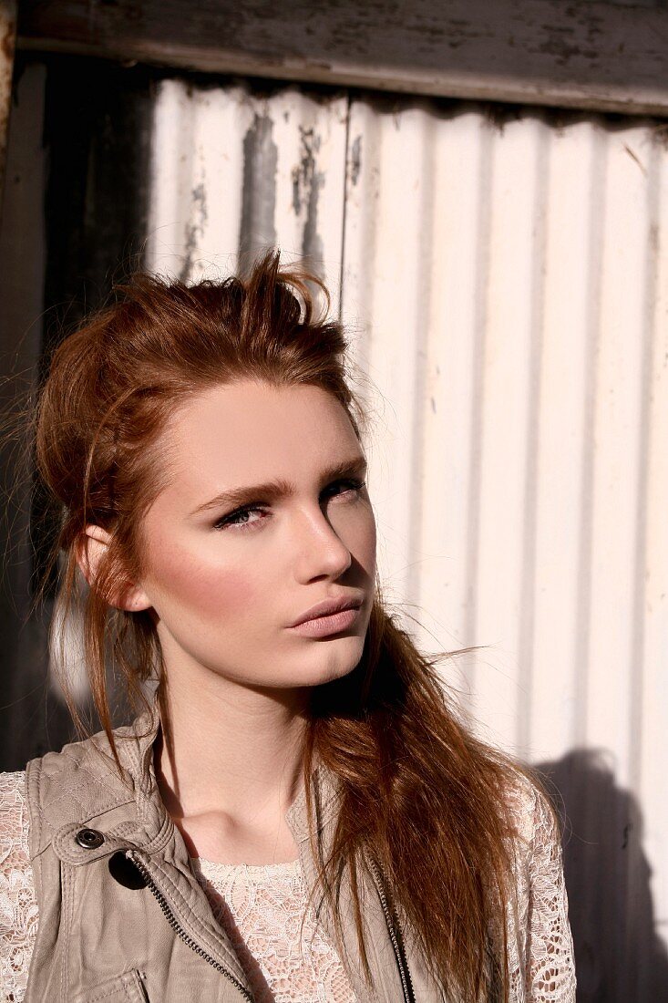 A young woman wearing a lace blouse and a leather gillet standing against a corrugated iron wall