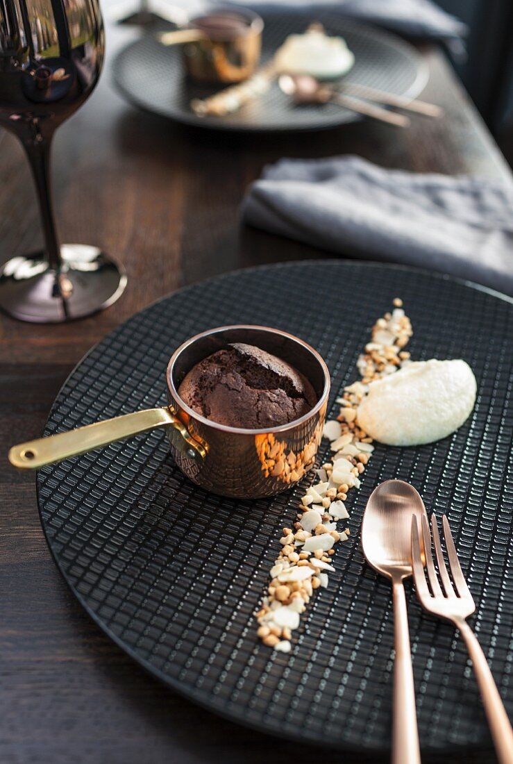 Schokoladensoufflé in Messingpfännchen und Vanilleschaumnocke auf Waffelteller