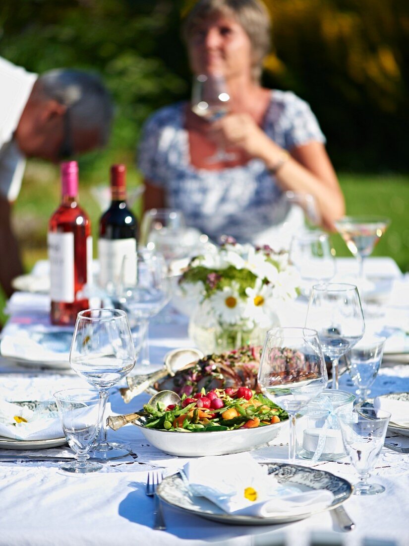 Gedeckter Tisch mit Schweinebraten, Salat und Wein zum Sommerfest