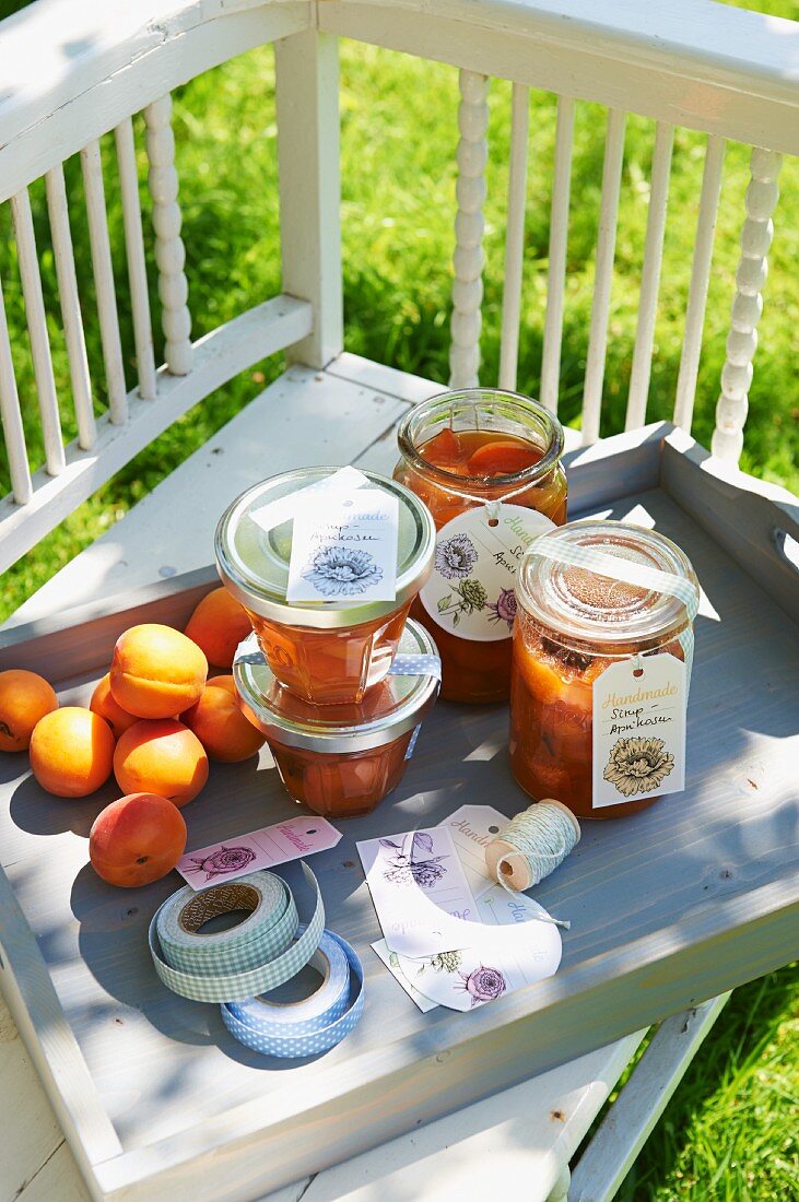 Jars of homemade apricot syrup on a wooden tray in a garden