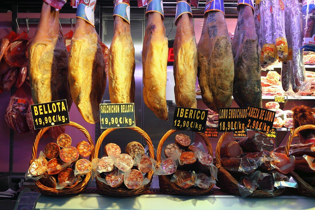 Iberischer Vorderschinken am Stück mit Knochen in Bellota-Qualität und verschiedene Salamis auf dem Markt in Bilbao, Baskenland, Spanien