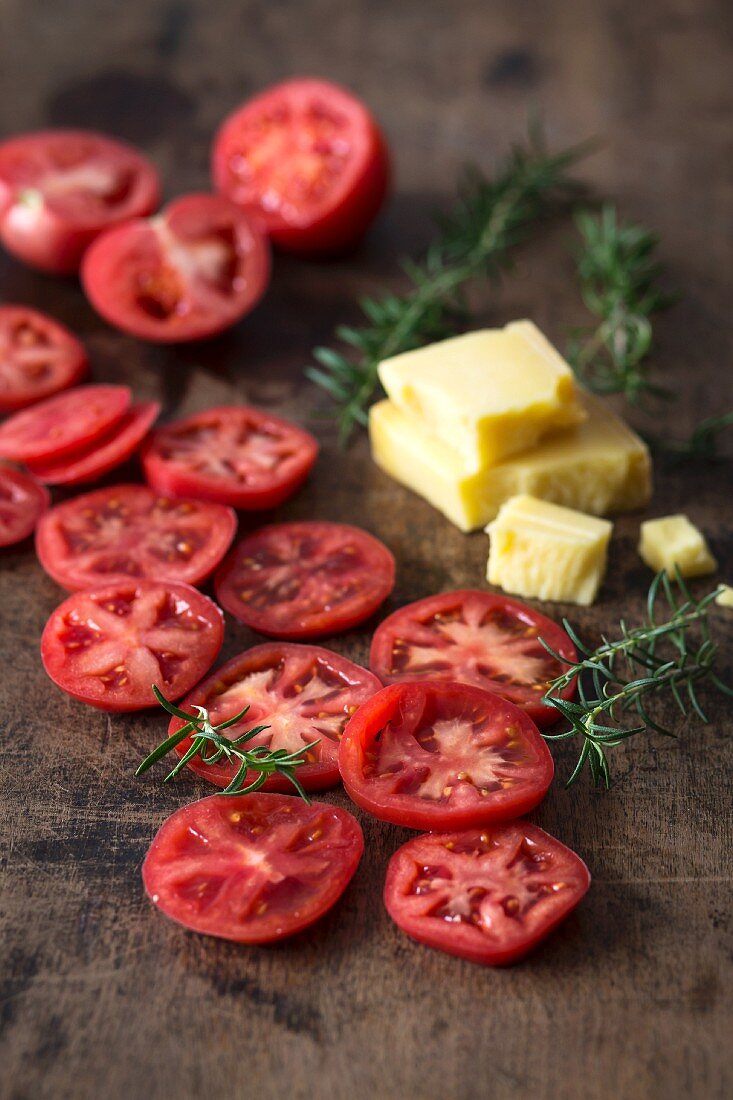 Slices of red tomatoes, pieces of cheese and fresh rosemary