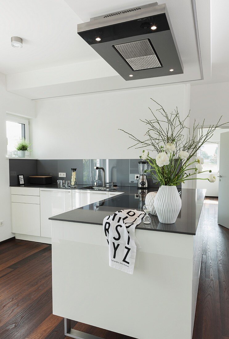 A white, contemporary, open-plan kitchen with an island counter under an extractor hood