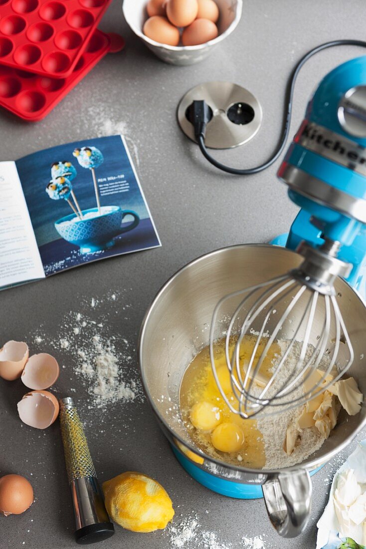 A kitchen machine with a mixing bowl and baking ingredients on a work surface with a built-in plug