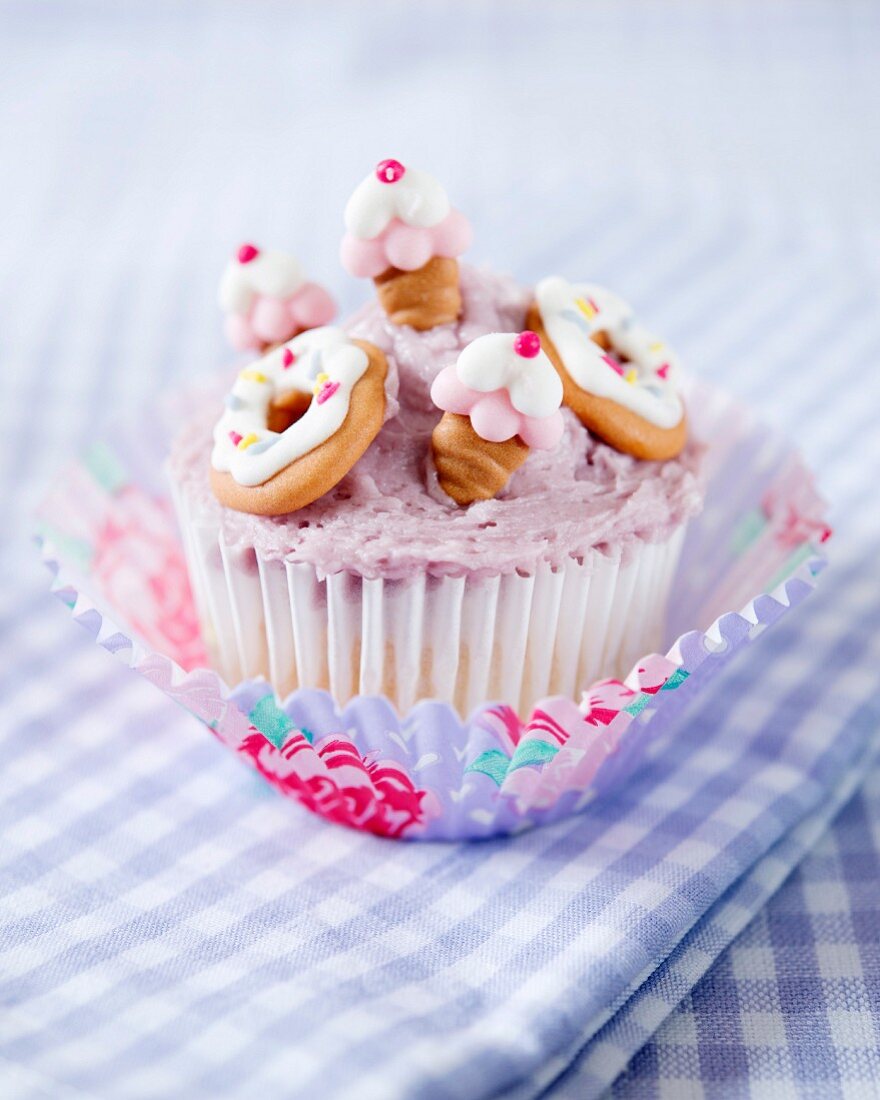 A cupcake decorated with blackcurrant butter cream and fondant cakes