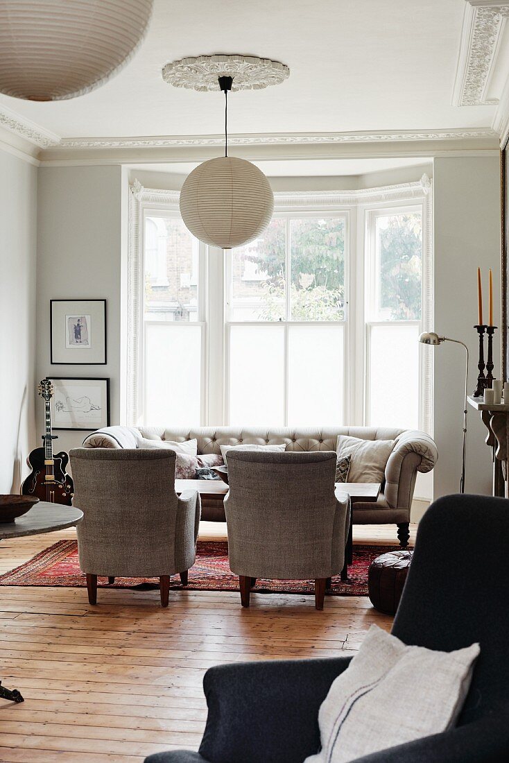 Traditional sofa set in living room in front of bay window below spherical lampshade hung from stucco ceiling