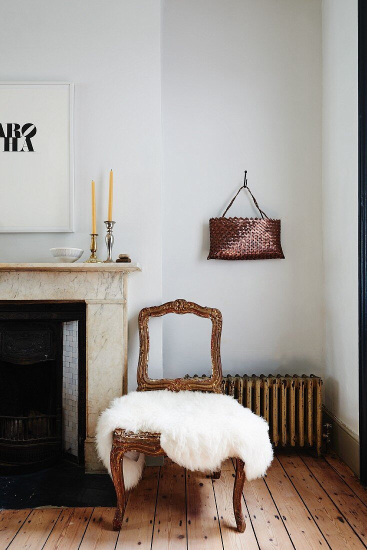 Vintage chairs with gilt wooden frame and white fur rug on seat next to fireplace