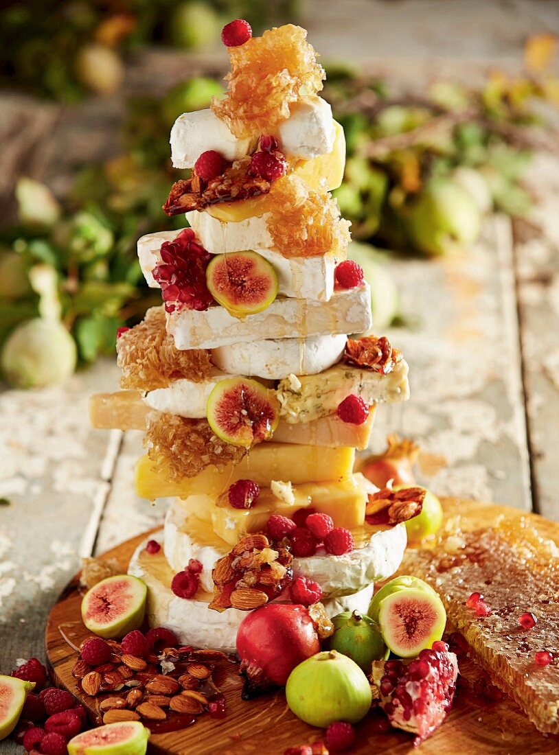 A stack of various slices of cheese, honeycomb, almonds and fruit