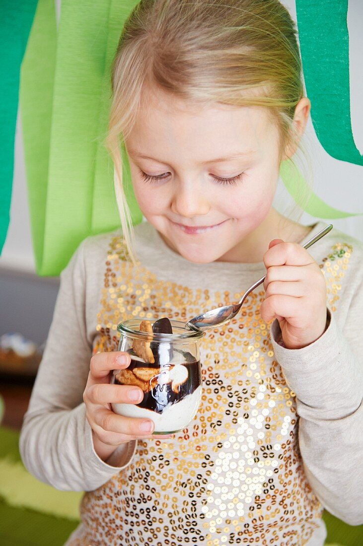 A little girl eating a quark dessert with bananas and chocolate sauce