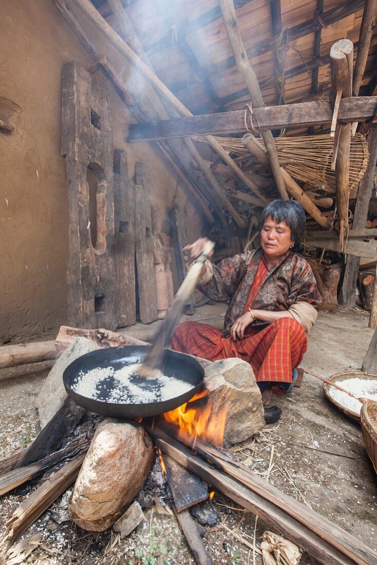 A woman from Thimphu wearing traditional clothing preparing rice in a simple wooden house in Bhutan