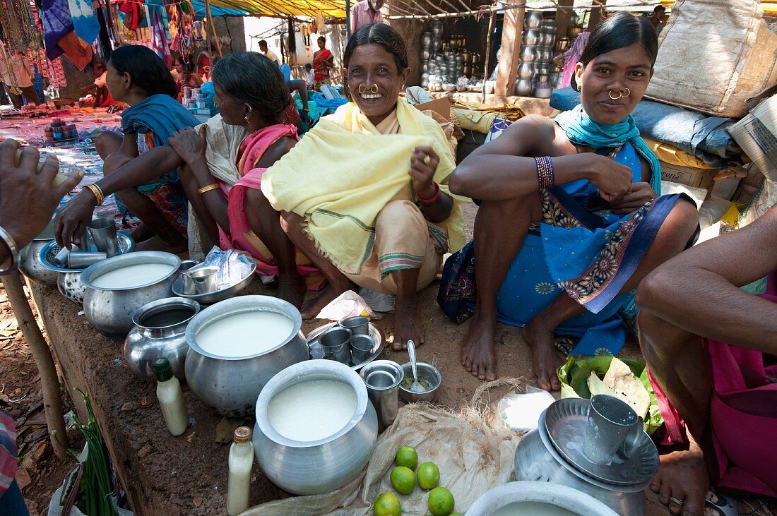 Smiling Mali tribeswomen with gold nose-rings selling yoghurt from metal pots at a weekly market at Guneipada, Orissa, India