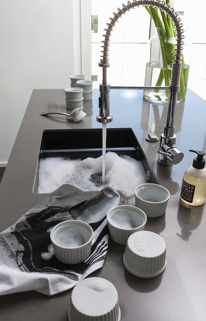 A kitchen block with a grey work surface: dessert bowls next to a ceramic sink with a professional shower attachment tap