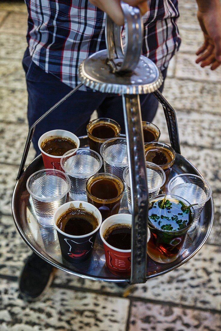 A man holding a tray of coffee, tea and water in the old city in Jerusalem, Israel