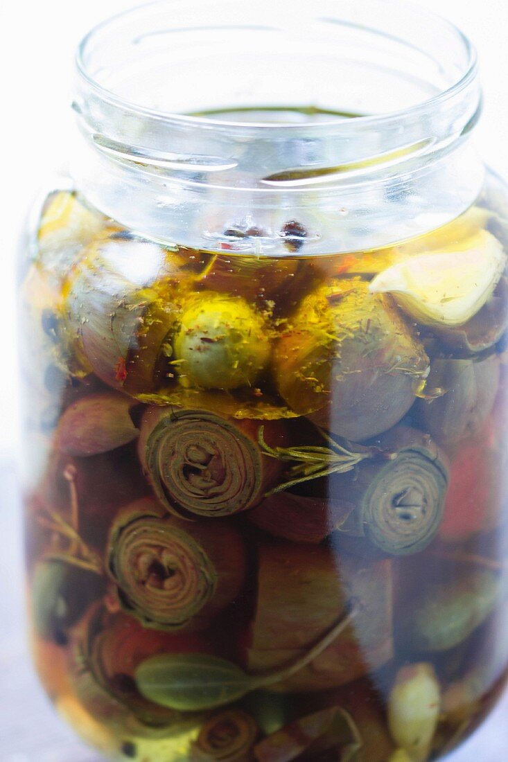 Pickled baby artichokes in a jar with caper fruits, bay leaves and rosemary