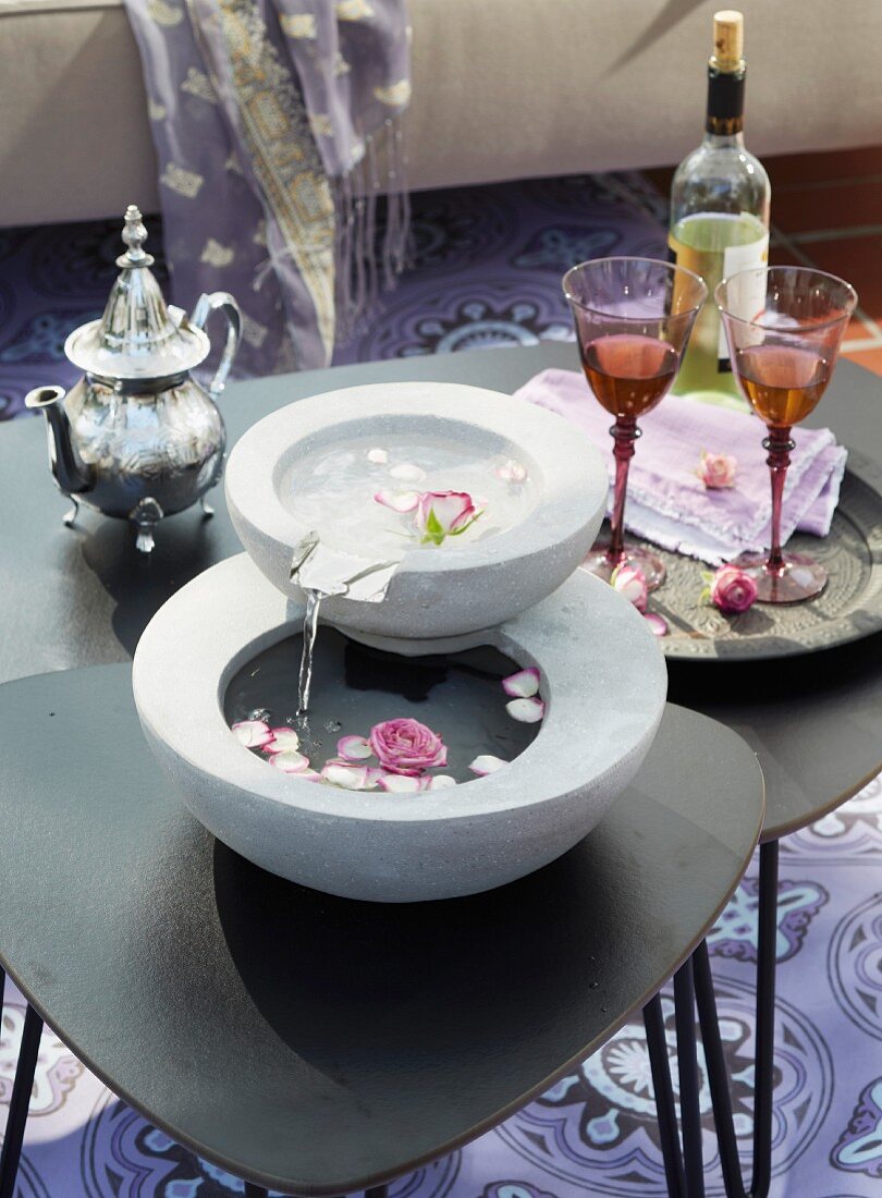 Oriental style: a mini fountain with rose petals and a silver teapot on a side table on a terrace