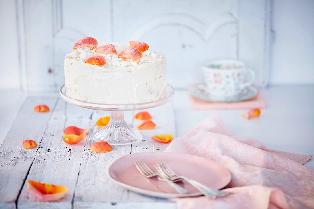 A cream cake with rose petals on a cake stand