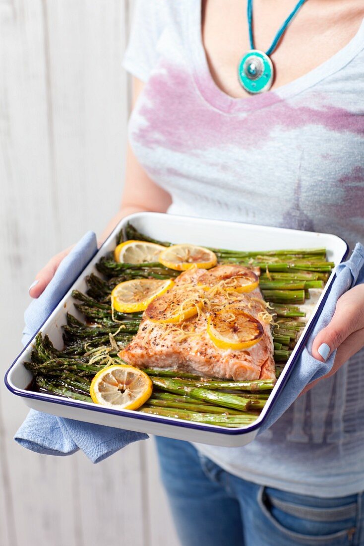 A woman serving baked salmon glazed in soya sauce with asparagus and lemon