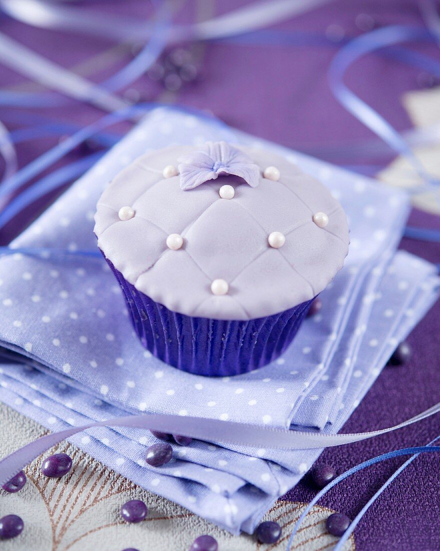 A purple fondant cupcake decorated with sugar pearls