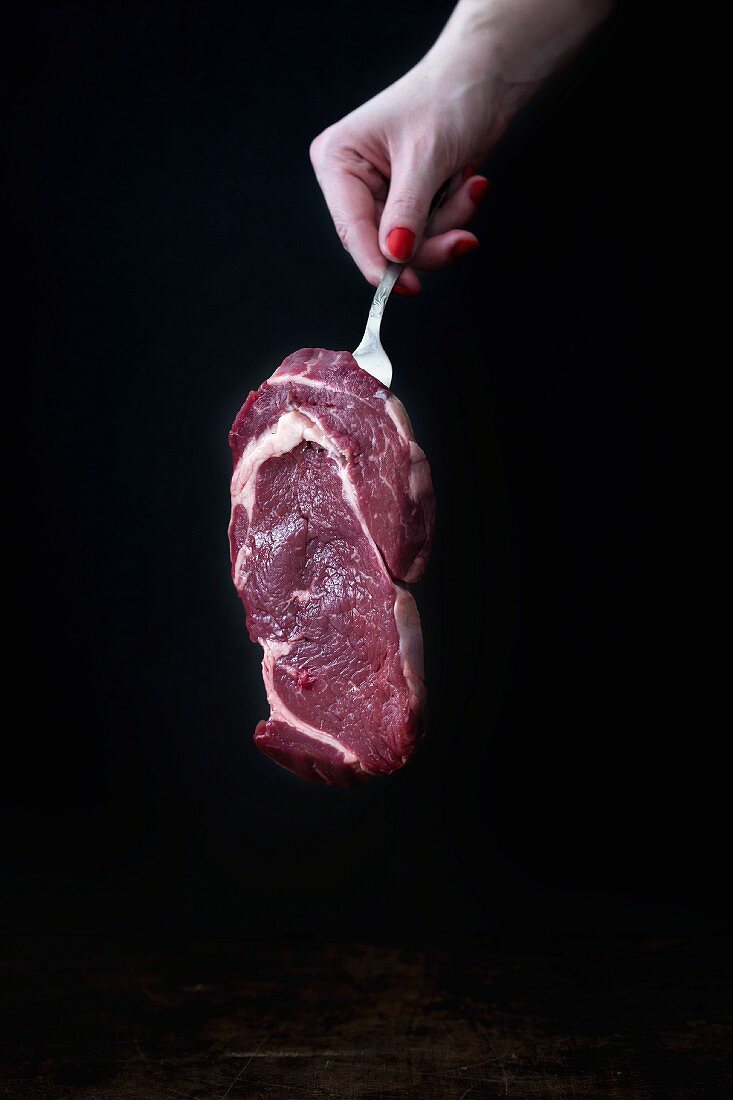 A woman hold a raw beef steak on a fork