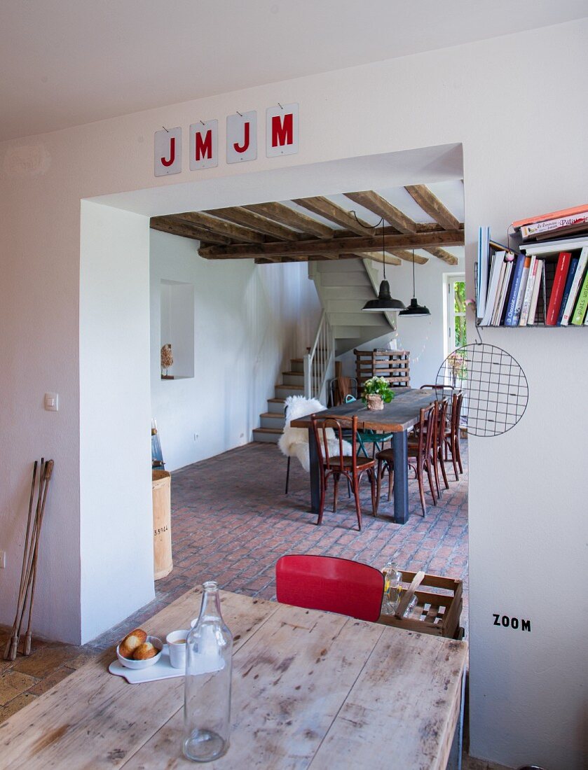 Wooden table in front of wide, open doorway with view of dining area and winding staircase in background