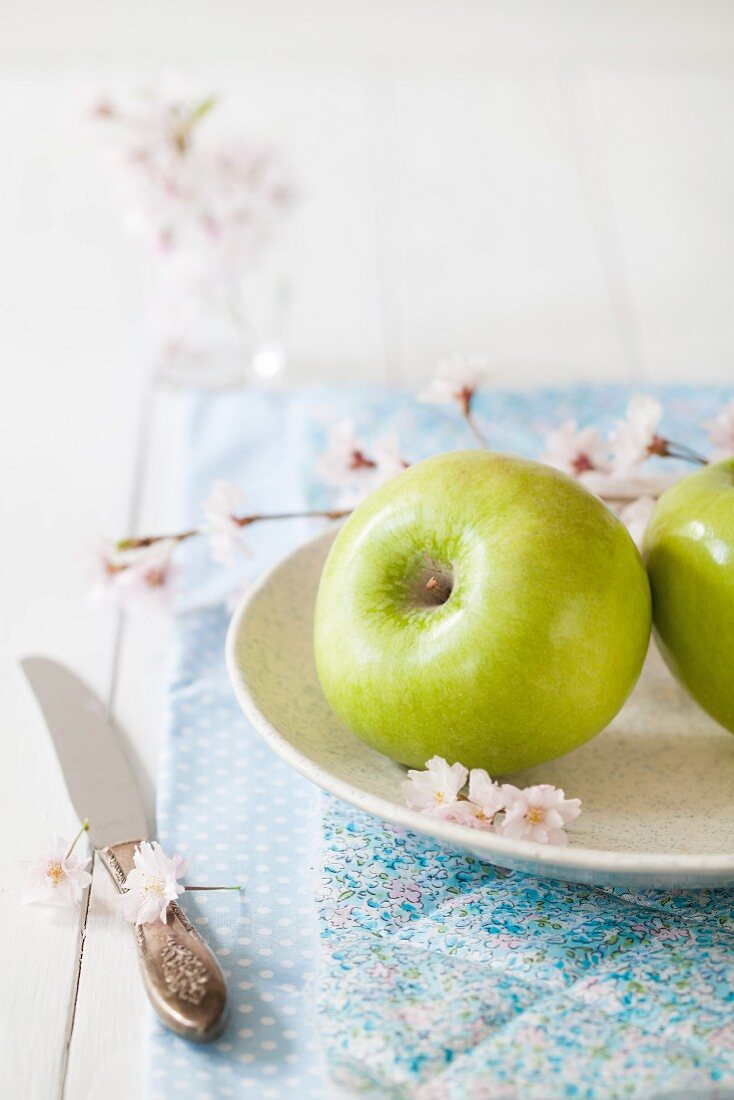 To green apples on a plate with apple blossom
