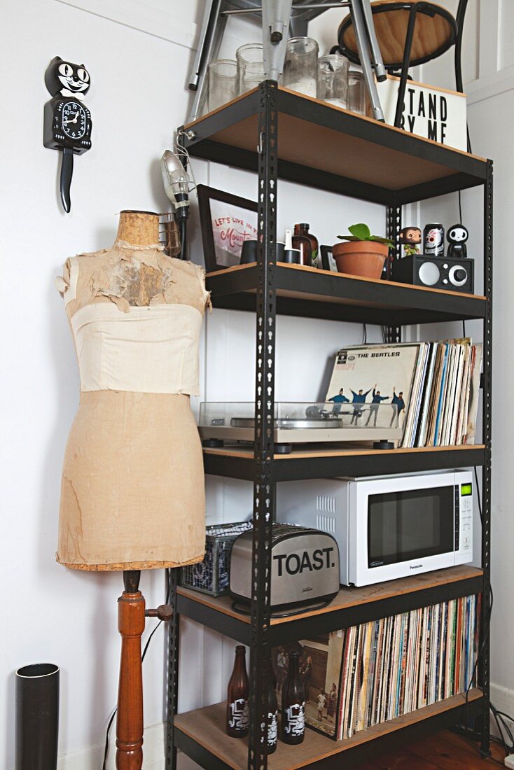 Records, toaster and microwave on black metal shelves next to tailors' dummy and cat-shaped clock