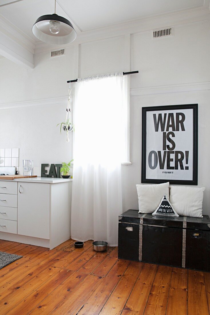 Poster with motto above vintage trunk next to window and simple kitchen counter in period apartment