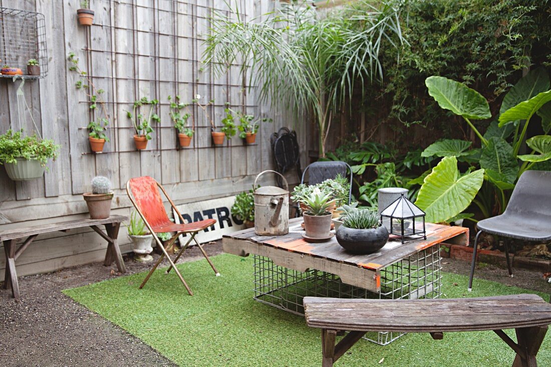Alte Holzbänke und DIY-Tisch im Innenhof mit vielen Pflanztöpfen und Kunstrasenteppich