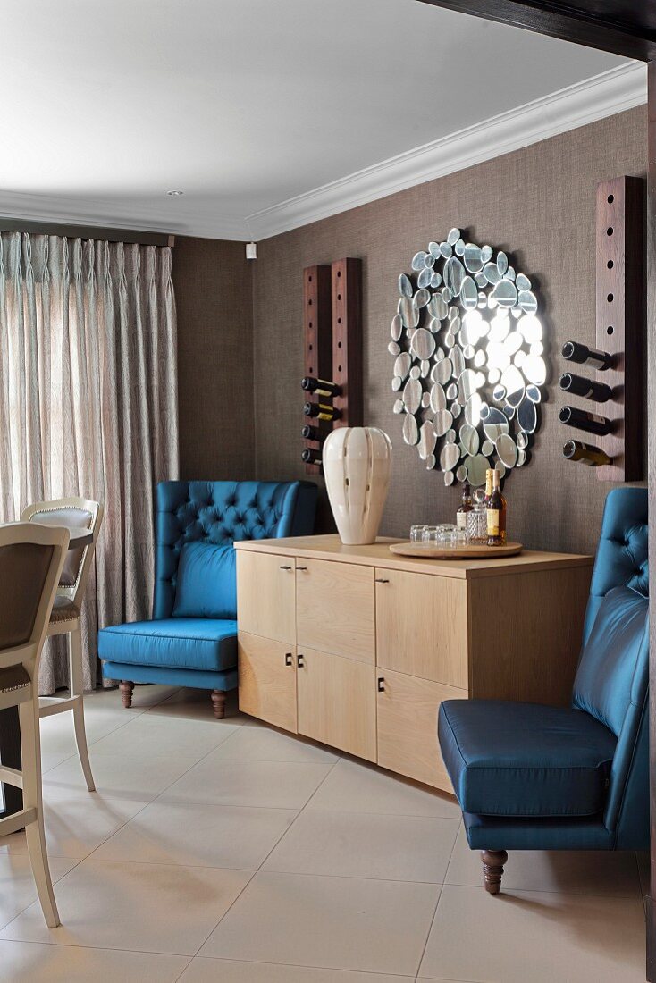 Armchairs with shiny blue upholstery flanking pale wooden sideboard in traditional interior