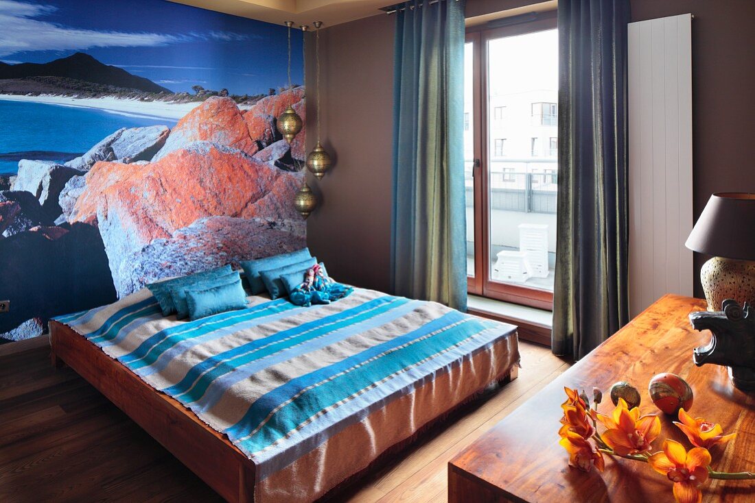 Double bed with striped bedspread against wall with poster mural of coastline and ocean