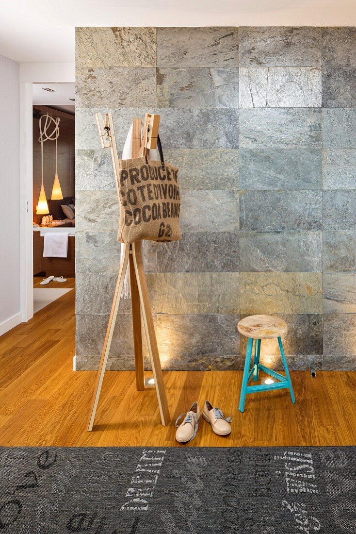 Tasche an Holzgarderobe, Hocker und Teppich mit Schriftprint vor Wand mit Natursteinfliesen