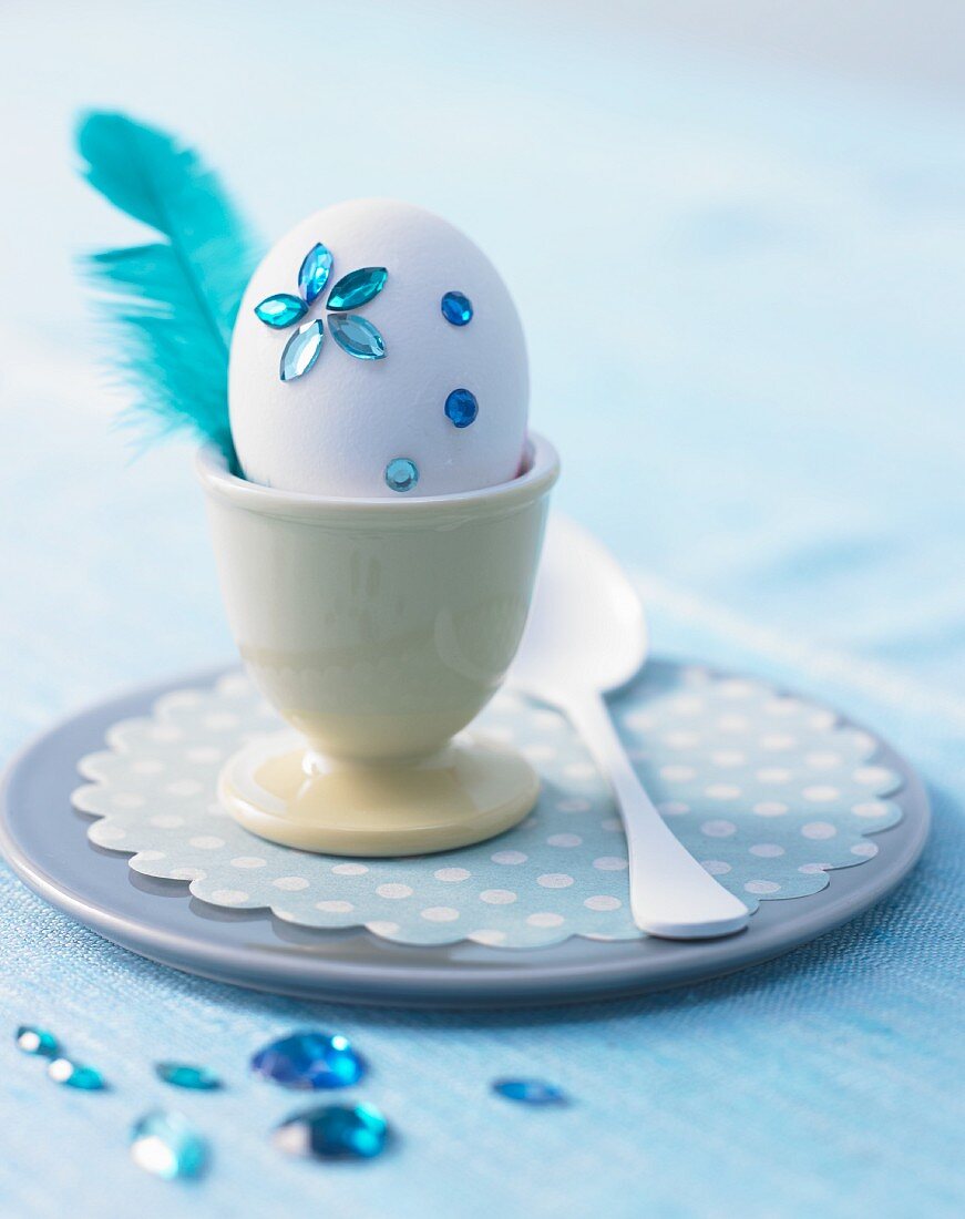 White egg decorated with blue rhinestones & feather in egg cup