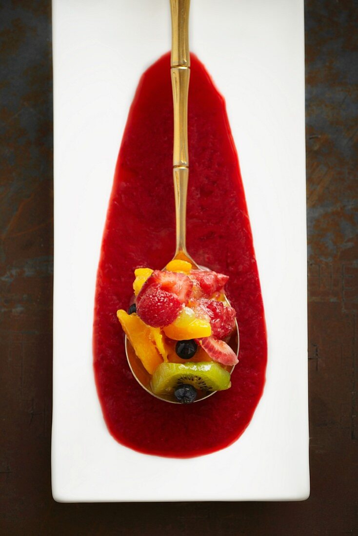 Fruit salad served on a golden spoon in a pool of sauce (seen from above)
