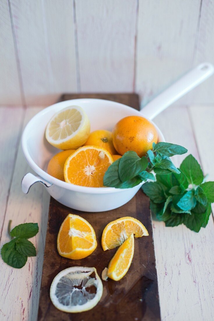 Orangen und Zitrone im Emaillesieb, frische Minze, Brett mit angeschnittener Zitrone und Orange