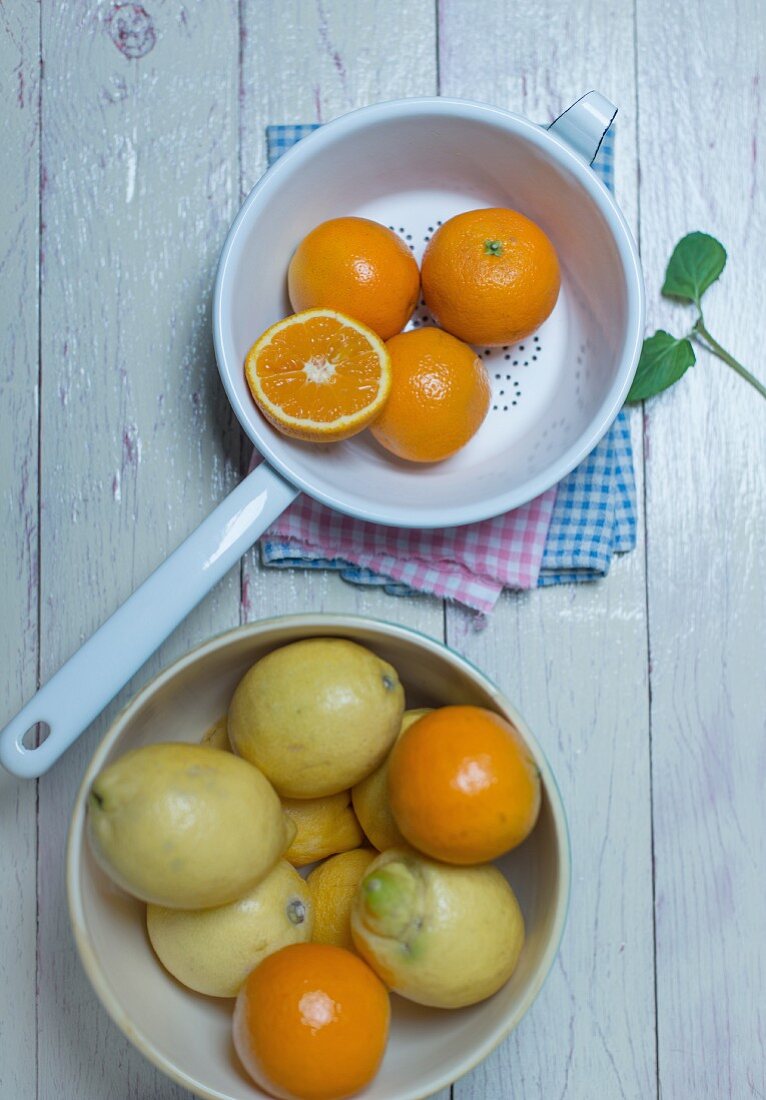 Oranges in an enamel colander, oranges and lemons in a porcelain bowl and fresh mint