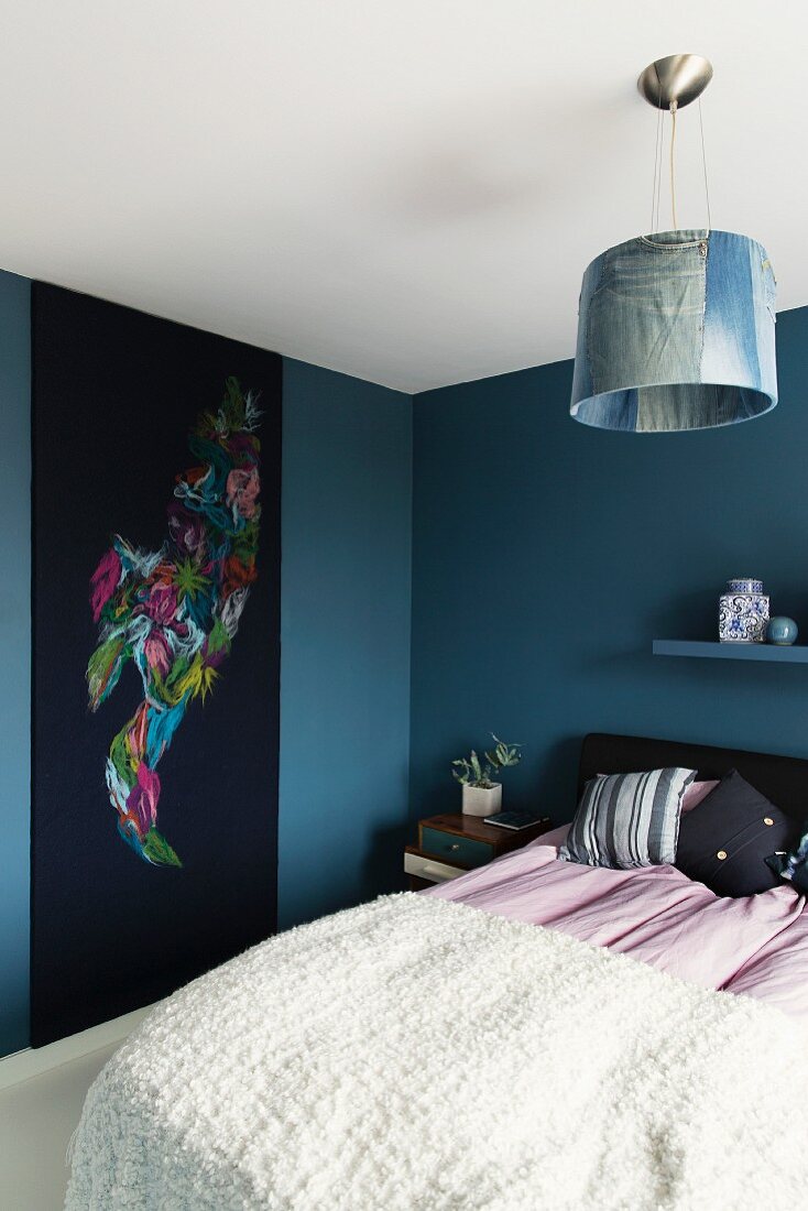 Bed with white cover and wall-hanging on blue-painted wall of modern bedroom