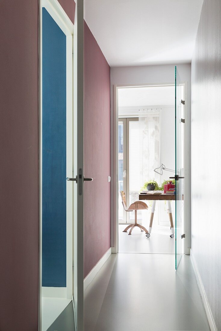 Narrow hallway leading to open glass door and view into modern study