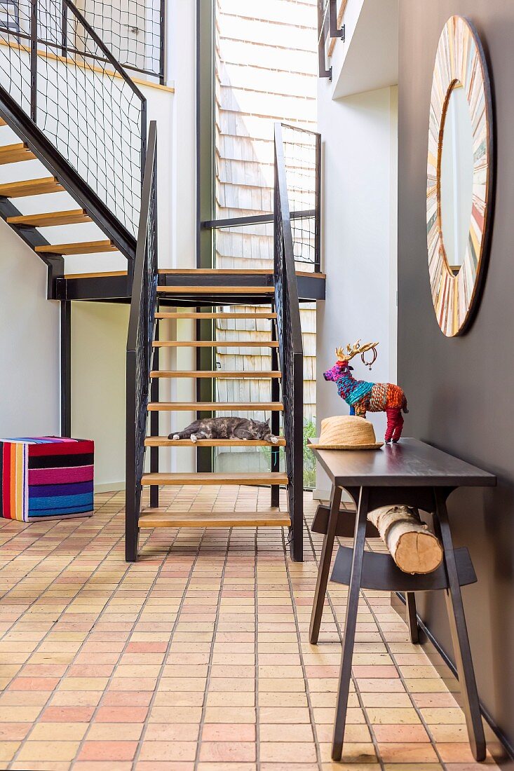 Dark table against brown wall in contemporary house with tiled floor and metal staircase with wooden treads