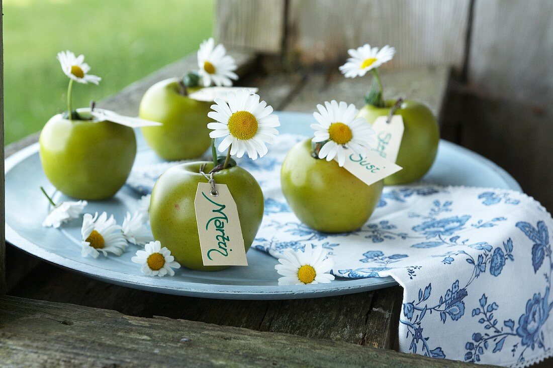Green apples with ox-eye daisies and name cards for decorating a summer dining table