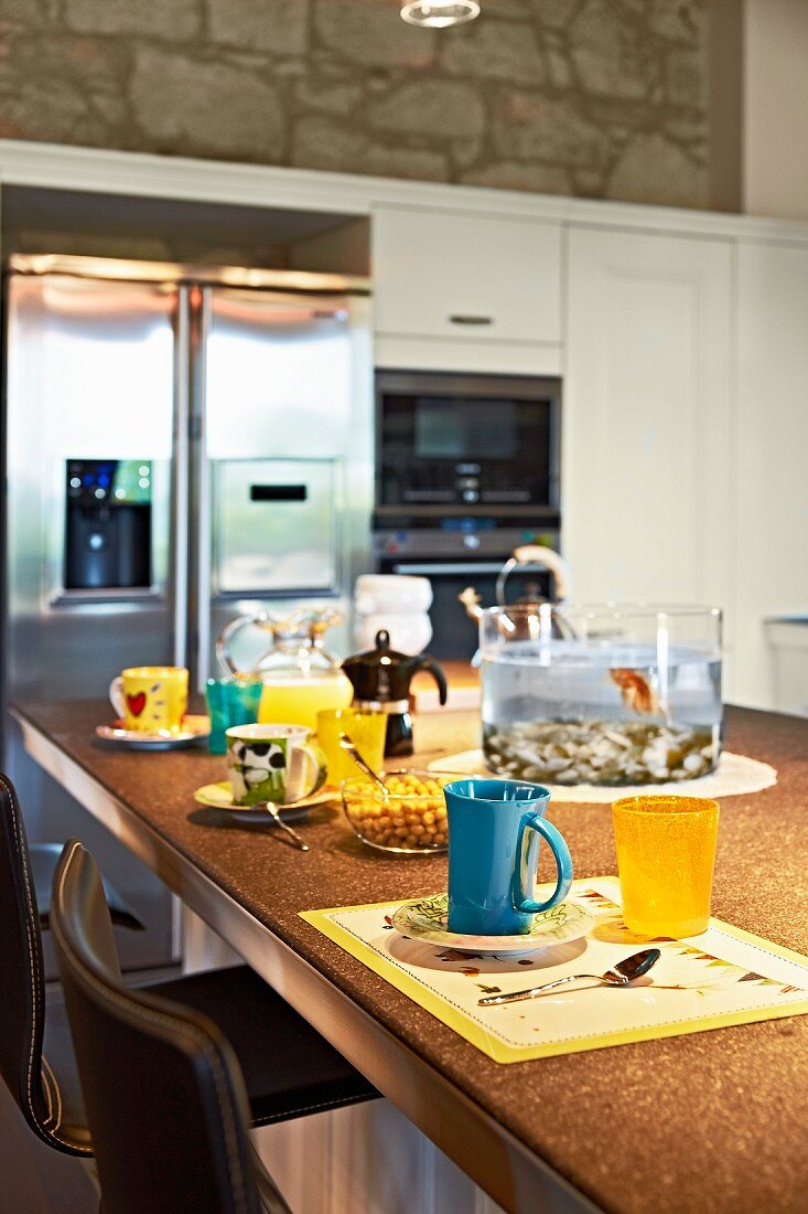 Colourful mugs and beakers on table in front of stainless steel fridge-freezer