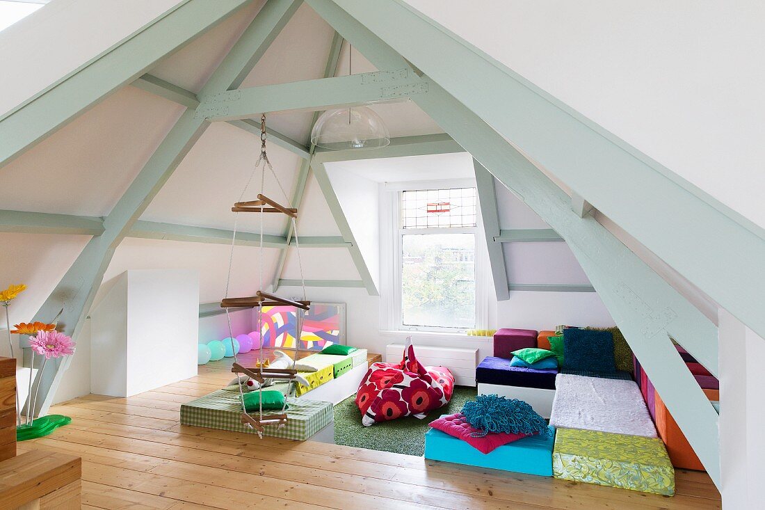 Colourful floor cushions and rope ladders suspended from wooden beams of exposed roof structure